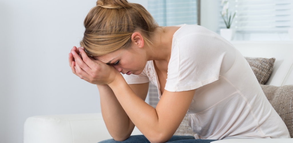 Upset woman sitting on a couch with her head in her hands, showing emotional distress or anxiety