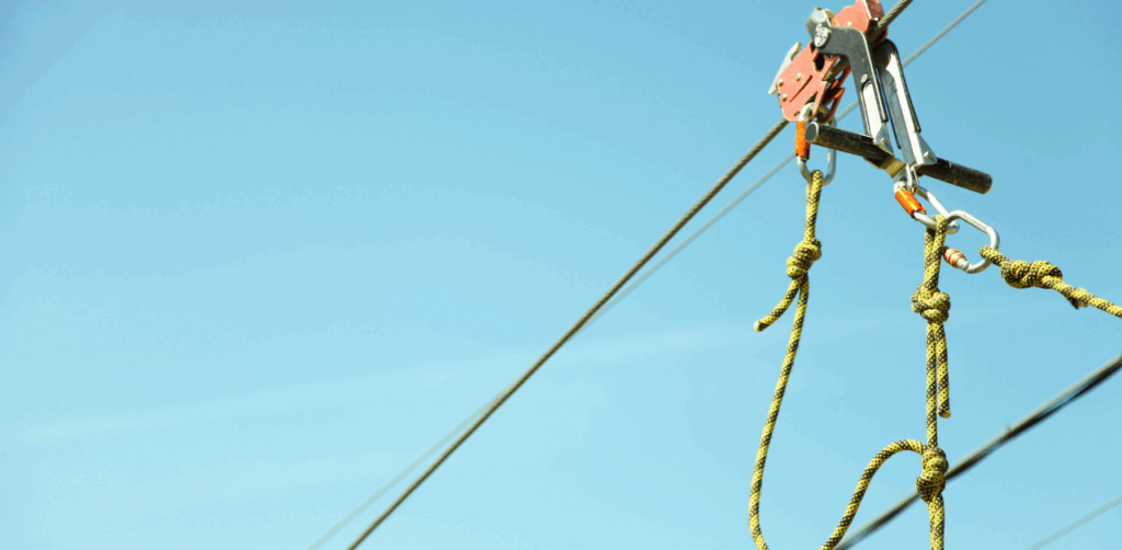 Close-up view of a zip line pulley and safety harness system suspended against a bright blue sky, highlighting the importance of secure equipment in zip line safety