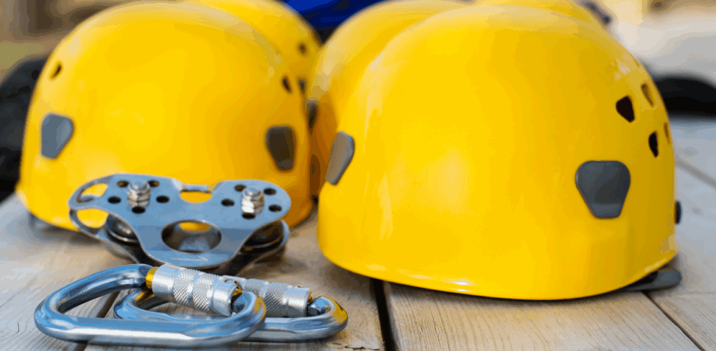 Group of bright yellow safety helmets, carabiners, and pulley gear laid out on a wooden surface, representing essential protective equipment for zip lining or rope-based adventure activities