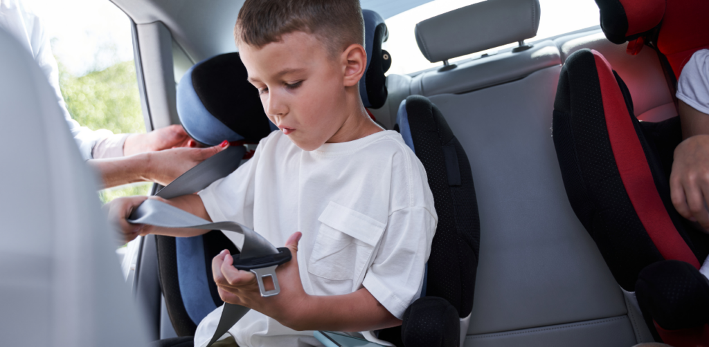 A young child in a car seat holding a seatbelt, with an adult helping to secure it