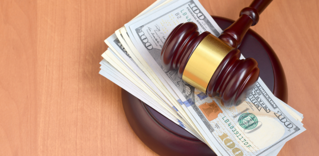 Judge's gavel resting on a stack of US hundred-dollar bills on a wooden surface