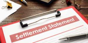 Clipboard holds a document titled “Settlement Statement” in bold red text, resting on a wooden desk with a pen and office supplies nearby, suggesting a legal or insurance payout agreement