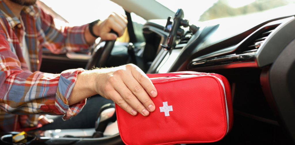 A man in a plaid shirt inside a car, placing a red first aid kit with a white cross into the glove compartment