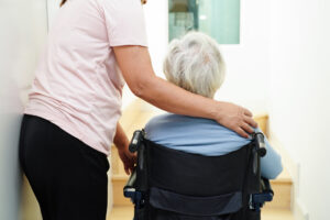 Senior woman on wheelchair with caregiver help support wall
