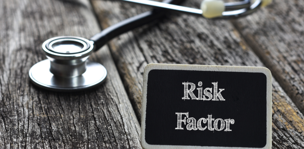 A stethoscope lying on a wooden surface next to a small chalkboard sign with the words Risk Factor