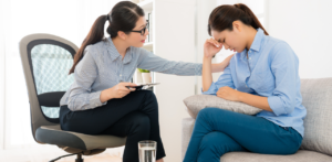 A woman comforting another woman who appears distressed, sitting on a couch in a bright room