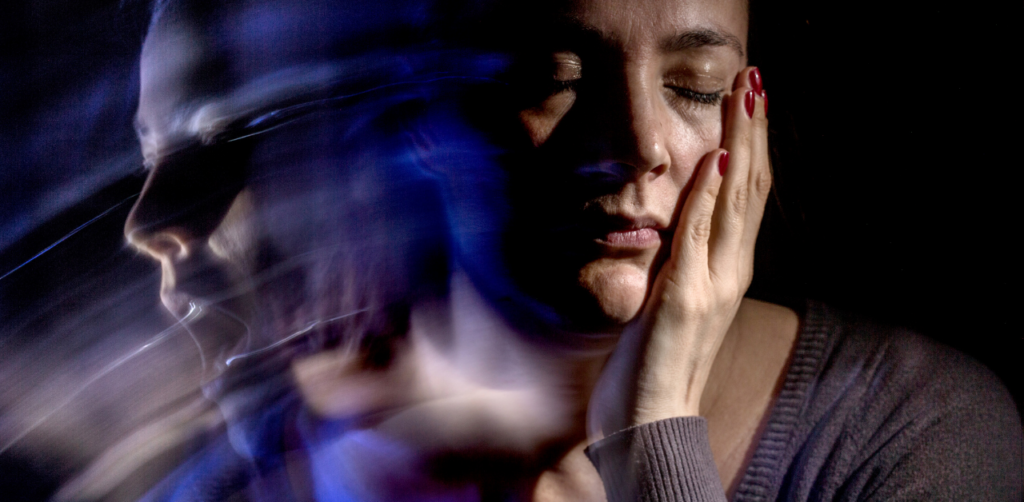 A woman with closed eyes holding her face, with a blurred double exposure effect that suggests emotional distress