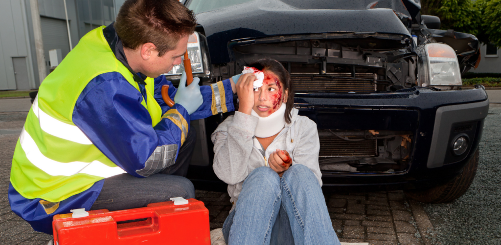 A paramedic attending to a woman with a neck brace and a head injury next to a car accident scene