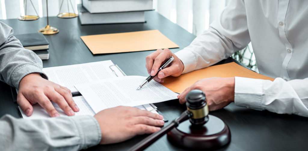 Two individuals at a desk reviewing and signing legal documents, with a gavel nearby, implying a legal or contractual discussion