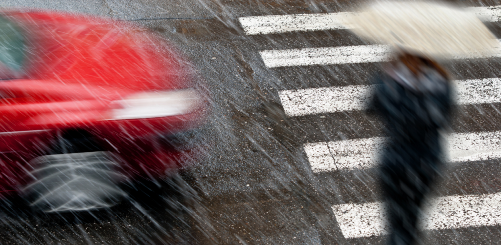 Blurry image of a red car and a person with an umbrella crossing a wet street during heavy rain