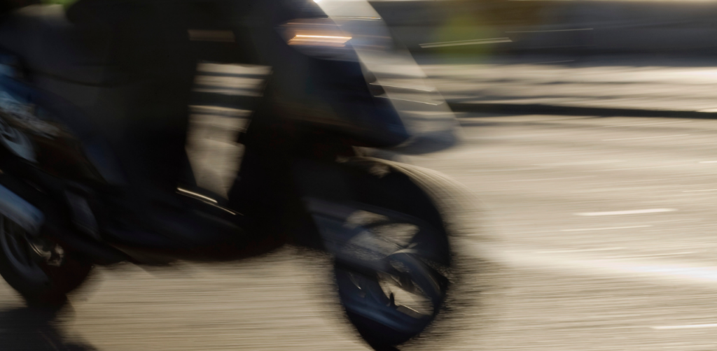 Blurry motion image of a scooter speeding down a road, with focus on the front wheel and faint headlight