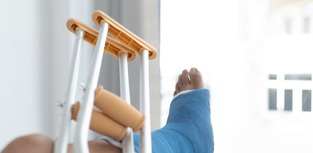 Close-up of a leg in a blue cast with crutches resting nearby, set in a bright room
