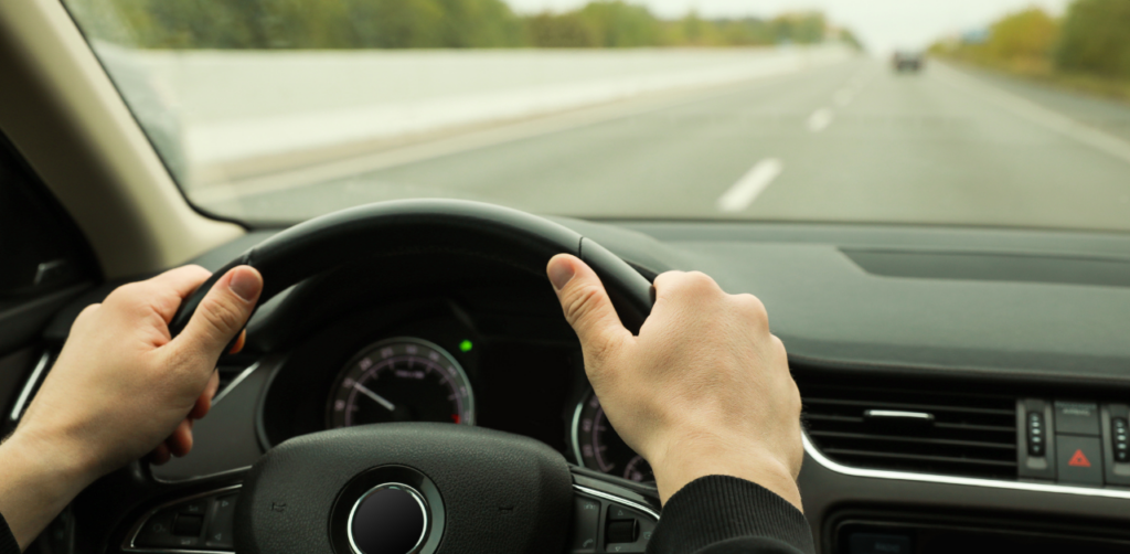 Close-up of hands on a car steering wheel, driving on an empty highway with a median and distant cars in view