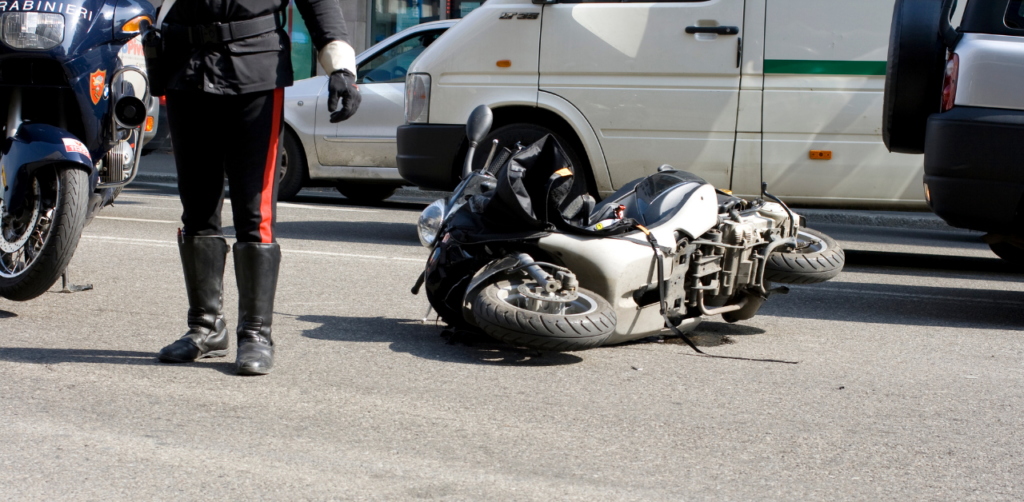 Police officer standing next to a fallen motorcycle on a city street, with parked vehicles in the background