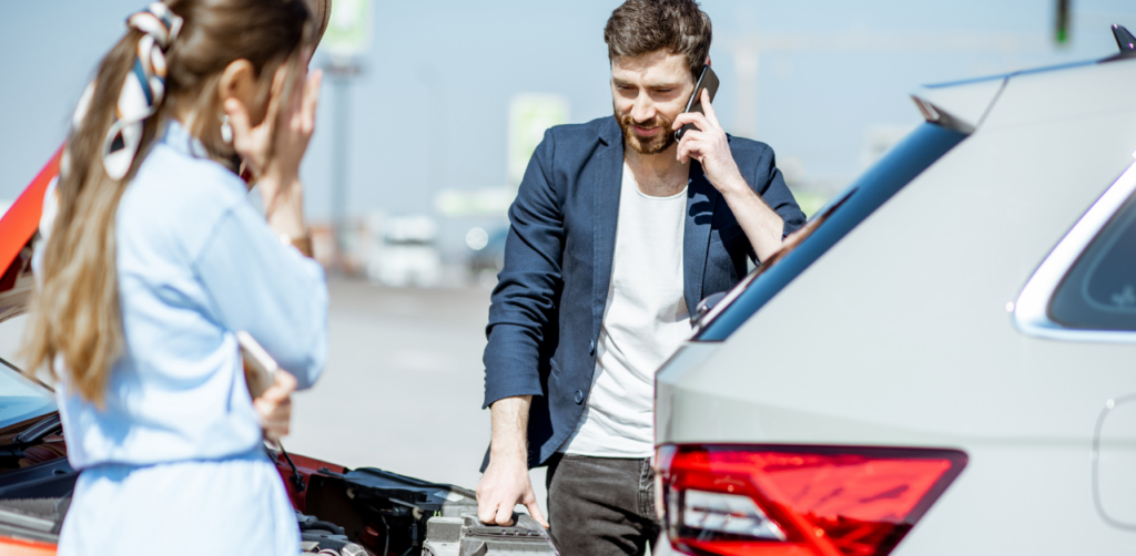 A man on his phone standing near two cars involved in a collision, with a woman holding her head in concern