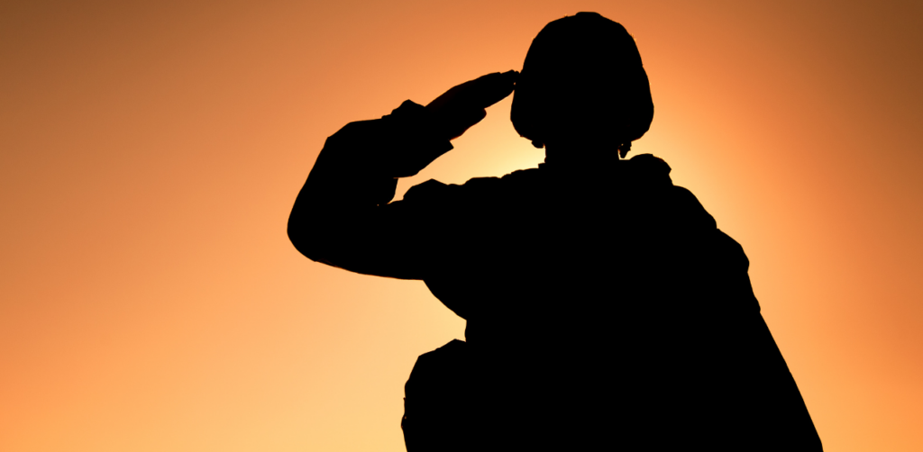A silhouette of a soldier saluting against an orange sunset background