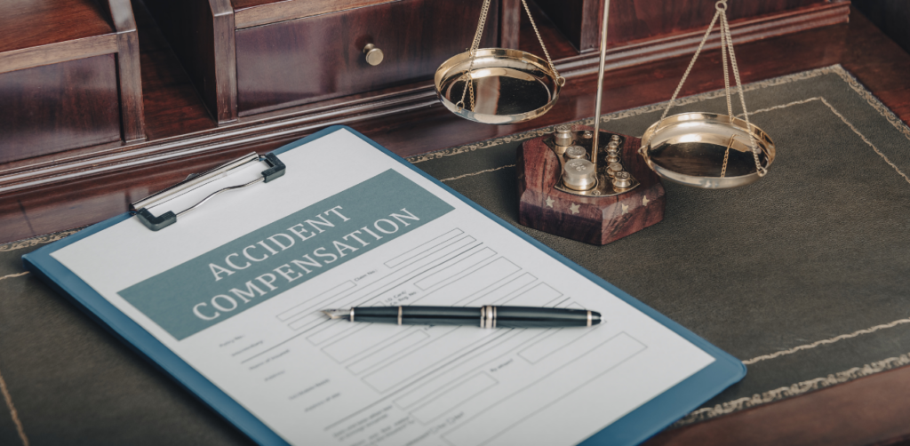 An accident compensation form with a pen placed on a desk next to a brass scale of justice