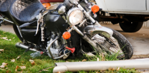 Damaged black motorcycle lying on grass with a broken pole nearby, indicating an accident