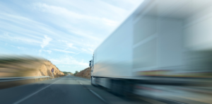 Blurred white truck speeds down a highway flanked by rocky terrain and a clear blue sky