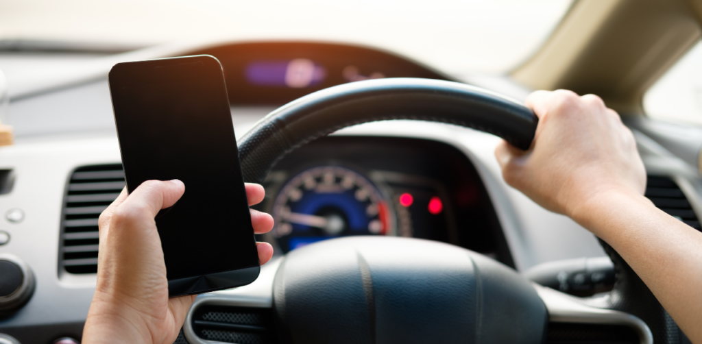 Driver holding a smartphone and steering the wheel inside a car
