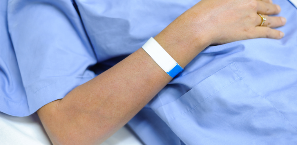 Person in a hospital gown rests, wearing a medical wristband on their arm