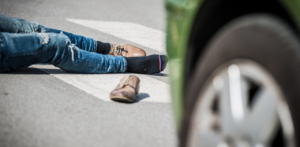 Person lying on the road near a car, with a shoe off, suggesting an accident