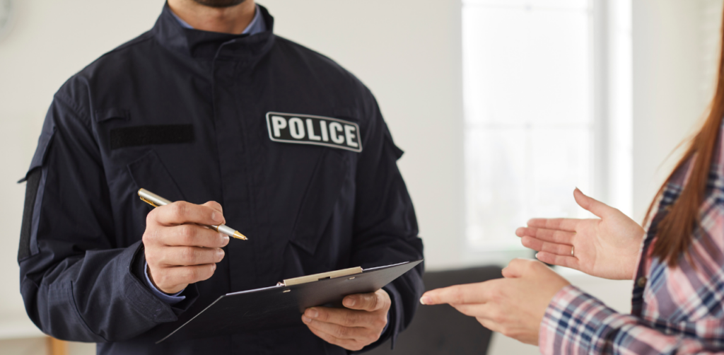 Police officer in uniform writes on a clipboard while speaking with a person gesturing in a plaid shirt