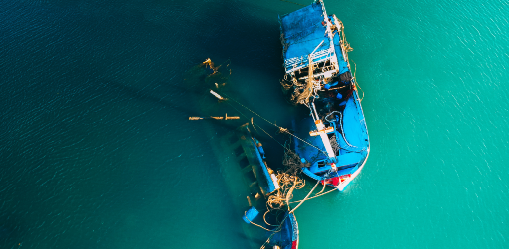Aerial view of a partially sunken blue fishing boat in turquoise waters
