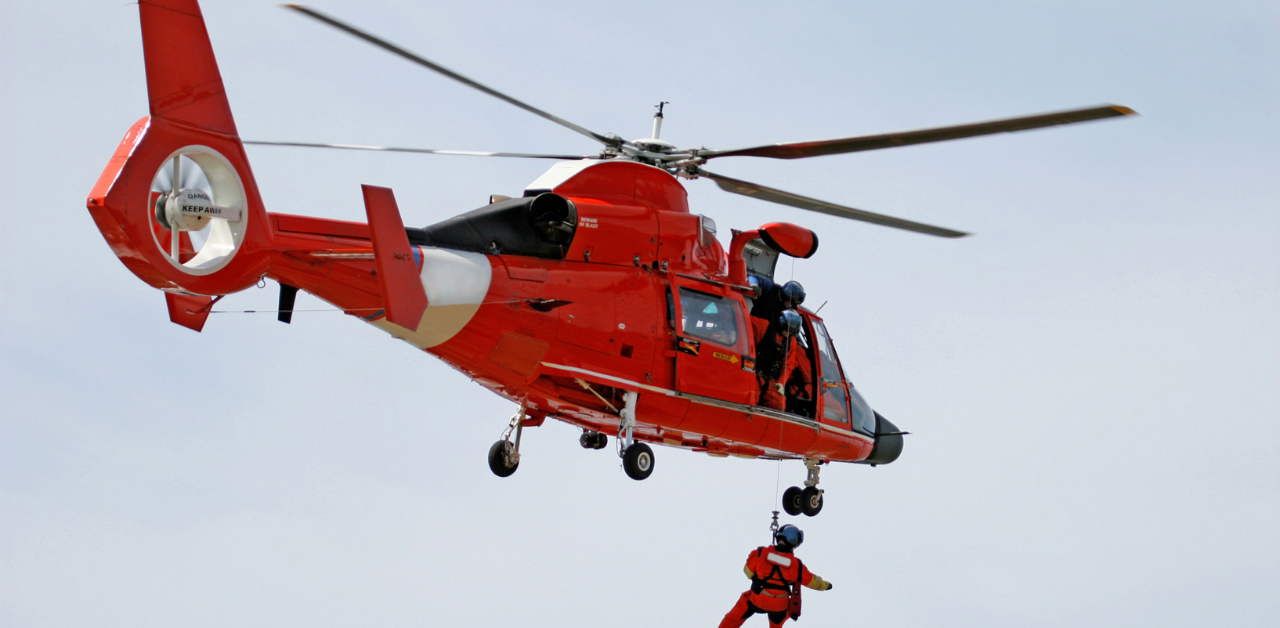 Bright red rescue helicopter mid-air with its rotor blades spinning, performing a search-and-rescue operation