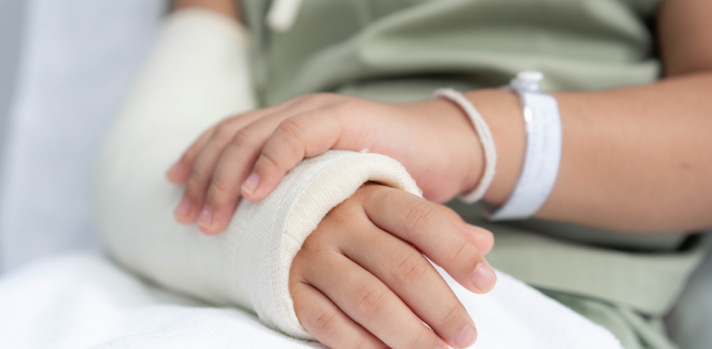 Close-up of a child's hands resting on a white cast covering their arm