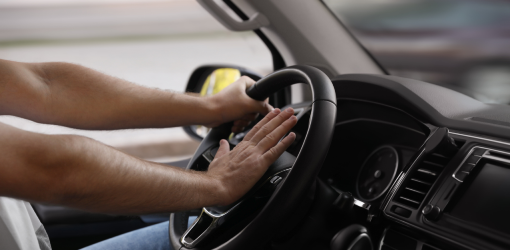 Driver pressing the car horn with both hands on the steering wheel, interior view of a moving vehicle