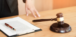 Gavel and legal document on a wooden desk with a person in formal attire standing behind it