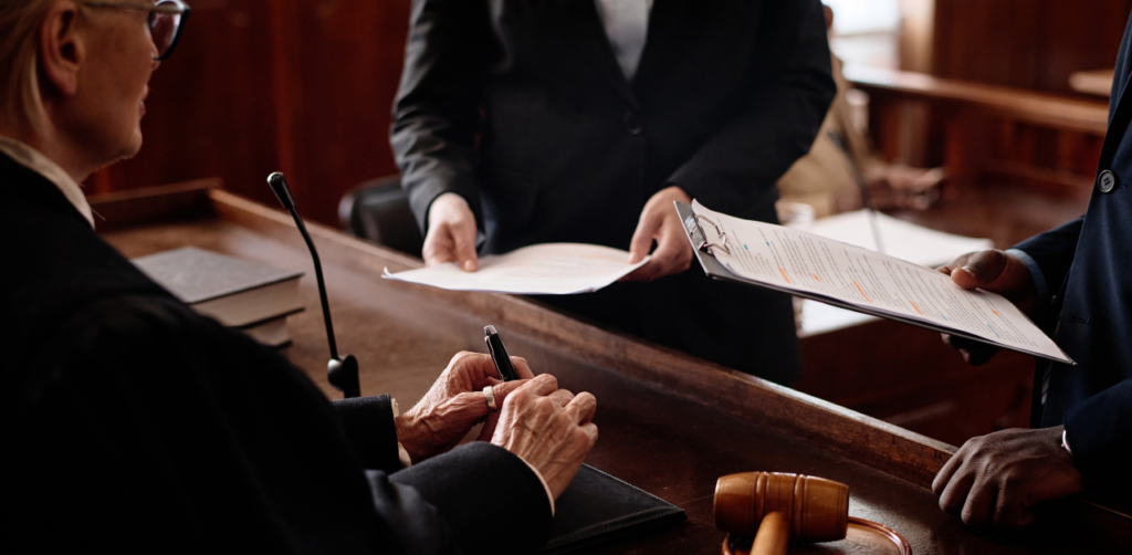 Judge at the bench reviewing legal documents handed over by two attorneys during a courtroom proceeding