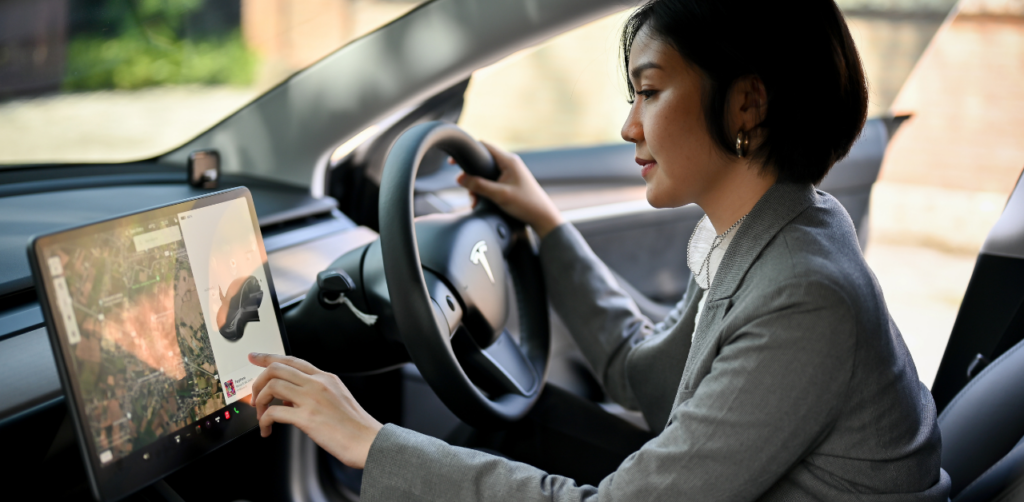 Woman in a gray blazer using the touchscreen dashboard of a Tesla while parked