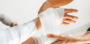Close-up of a person's injured arm being wrapped in white medical bandages by a caregiver