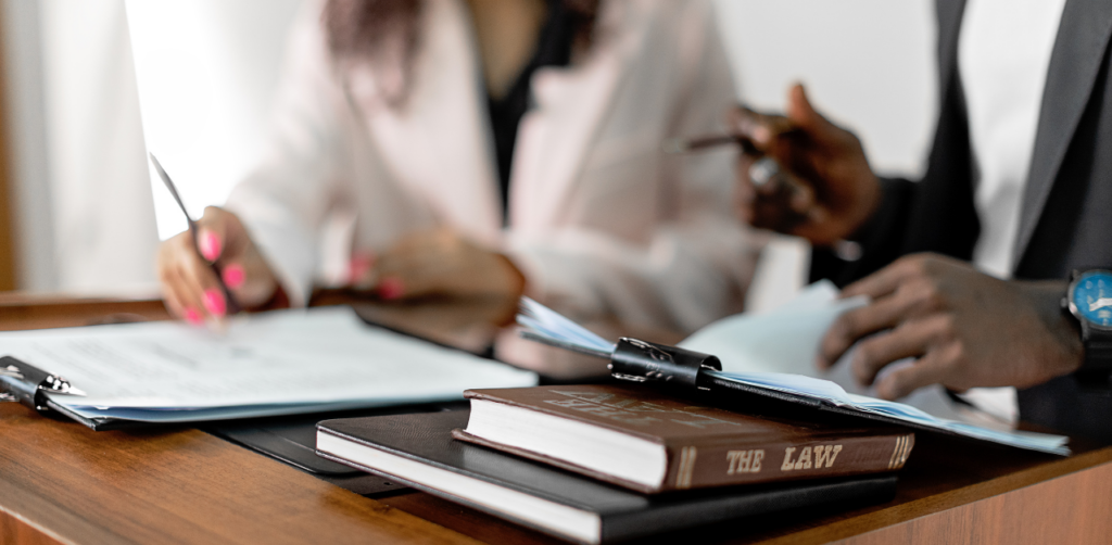 Close-up of two professionals reviewing documents at a wooden desk, with a law book and clipboard in focus