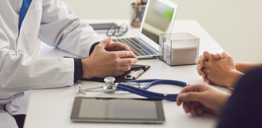 Doctor consulting with a patient at a desk, with medical tools and a laptop nearby
