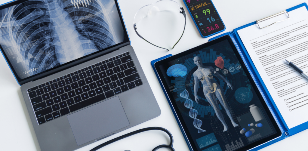 Flat lay of medical tools, a laptop with X-ray, tablet with 3D anatomy, and patient form on a desk