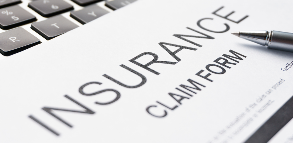 Insurance claim form with a silver pen resting on it, placed over a laptop keyboard, ready for completion