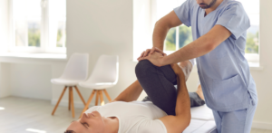 Male physical therapist stretching a patient’s bent leg during a rehab session in a bright room