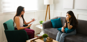 Therapist talking to a young woman crying into a tissue during a counseling session on a gray couch