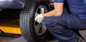 Auto technician in gloves crouches while installing or inspecting a tire on a vehicle in a garage