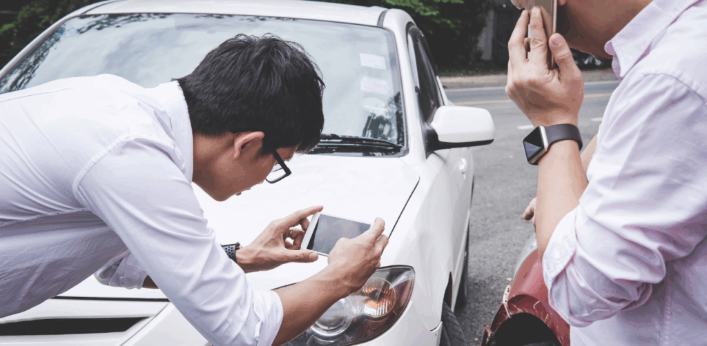 Man photographs car damage with smartphone while another calls after a minor accident