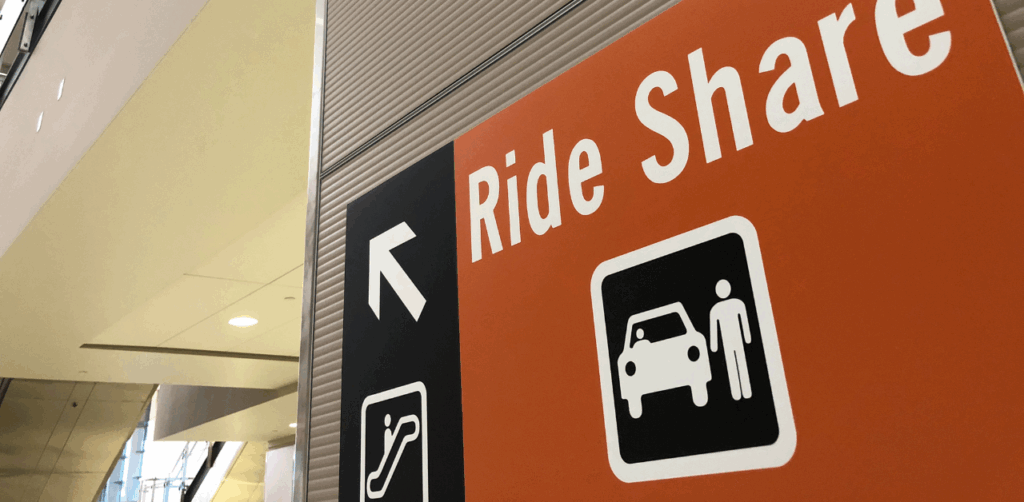Orange airport sign with white text reading “Ride Share” and icons for a car, person, and escalator