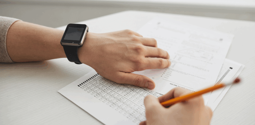 Person wearing a smartwatch filling out a multiple-choice test sheet with a pencil at a desk
