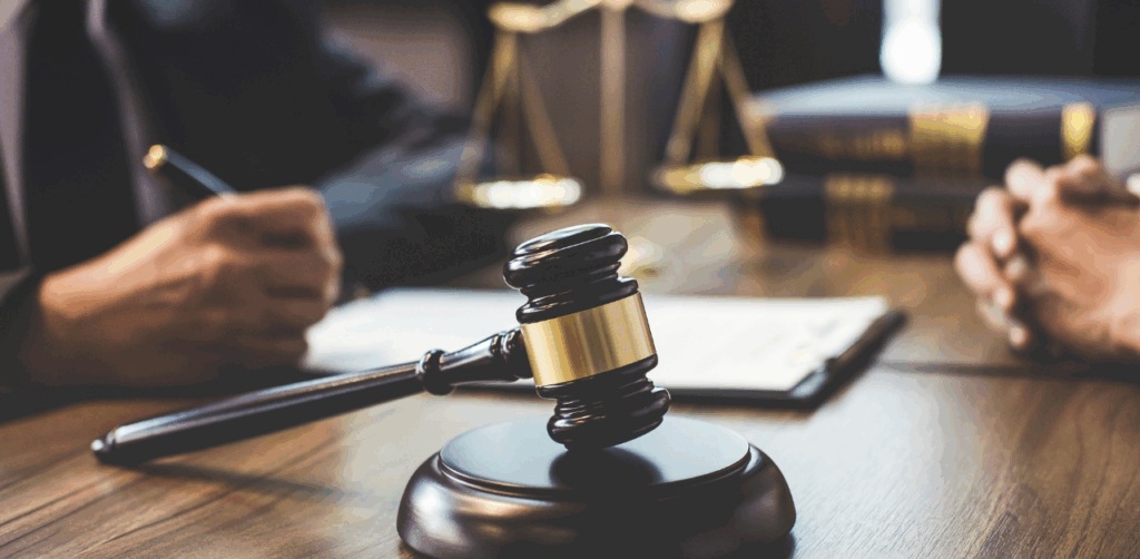 Close-up of a judge’s gavel on a desk with two people discussing legal documents in the background