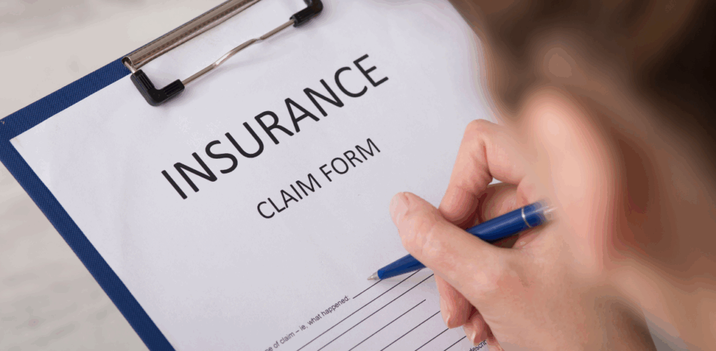 Close-up of a person filling out an insurance claim form on a clipboard with a blue pen