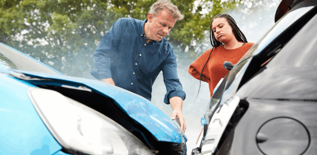 Man and woman examining damage after a collision between a blue car and a black car, with smoke rising from the vehicles