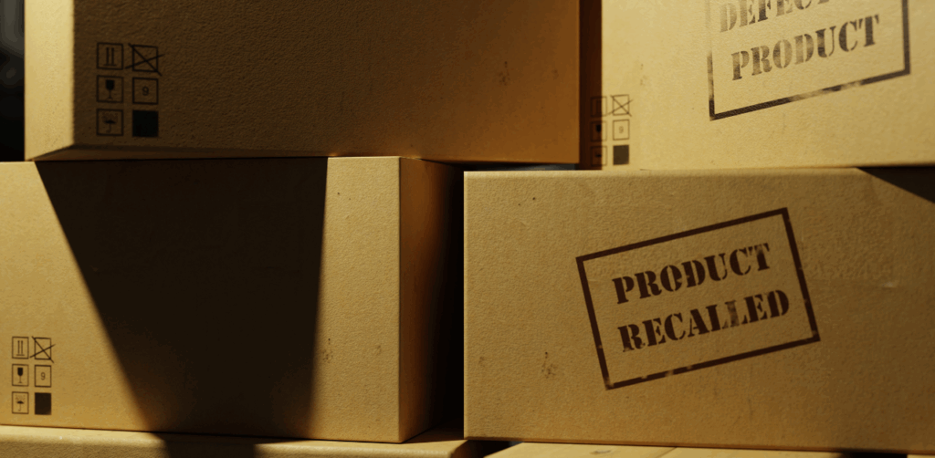 Stacks of cardboard boxes with bold “PRODUCT RECALLED” and “DEFECTIVE PRODUCT” stamps