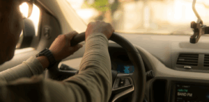 A driver grips the steering wheel with both hands while navigating a vehicle on a sunny day